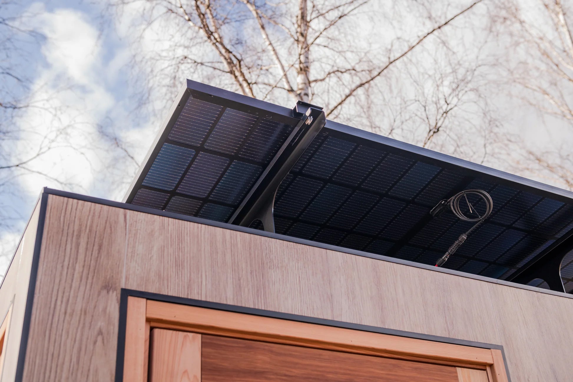 Black solar panel roof on modern outdoor sauna with wood siding and copper door frame