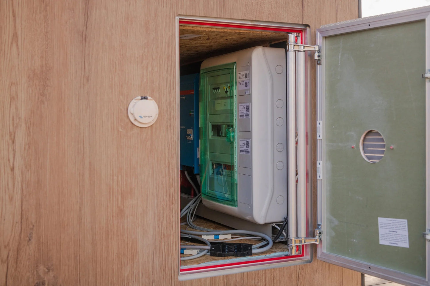 Open electrical panel with white distribution box, green door, and red frame mounted on wood wall