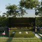 Modern outdoor sauna with black frame and frosted glass panels in garden setting surrounded by hedges and flowering plants