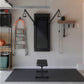 Home gym setup with black Tonal smart fitness machine mounted on wall, orange and gray ladder, black weight bench, wooden she