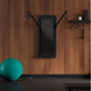 Black wall-mounted smart home gym with adjustable cable arms on wood plank wall, displayed in home gym setting with teal exer