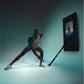 Man in white tank top and black shorts doing a lunge exercise with Tonal 2 smart home gym against teal background