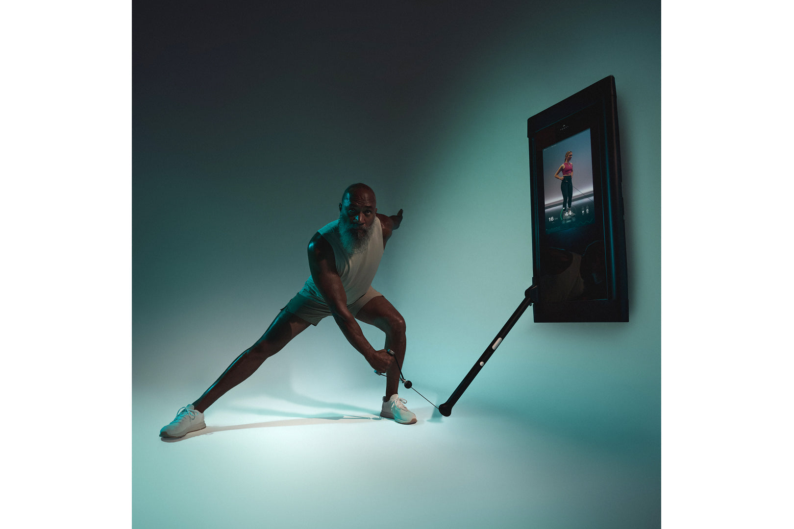 Man in white tank top and black shorts doing a lunge exercise with Tonal 2 smart home gym against teal background