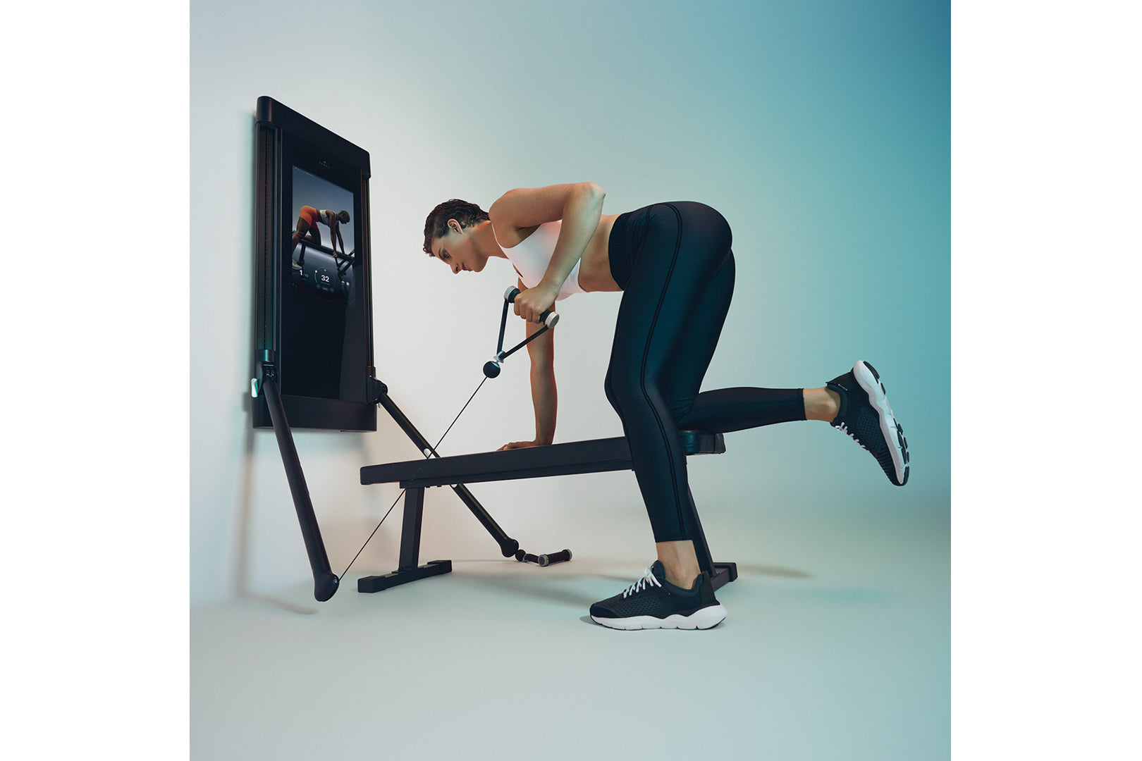 Person using black Tonal 2 Smart Home Gym with mounted display screen, performing strength training exercise with cable attac