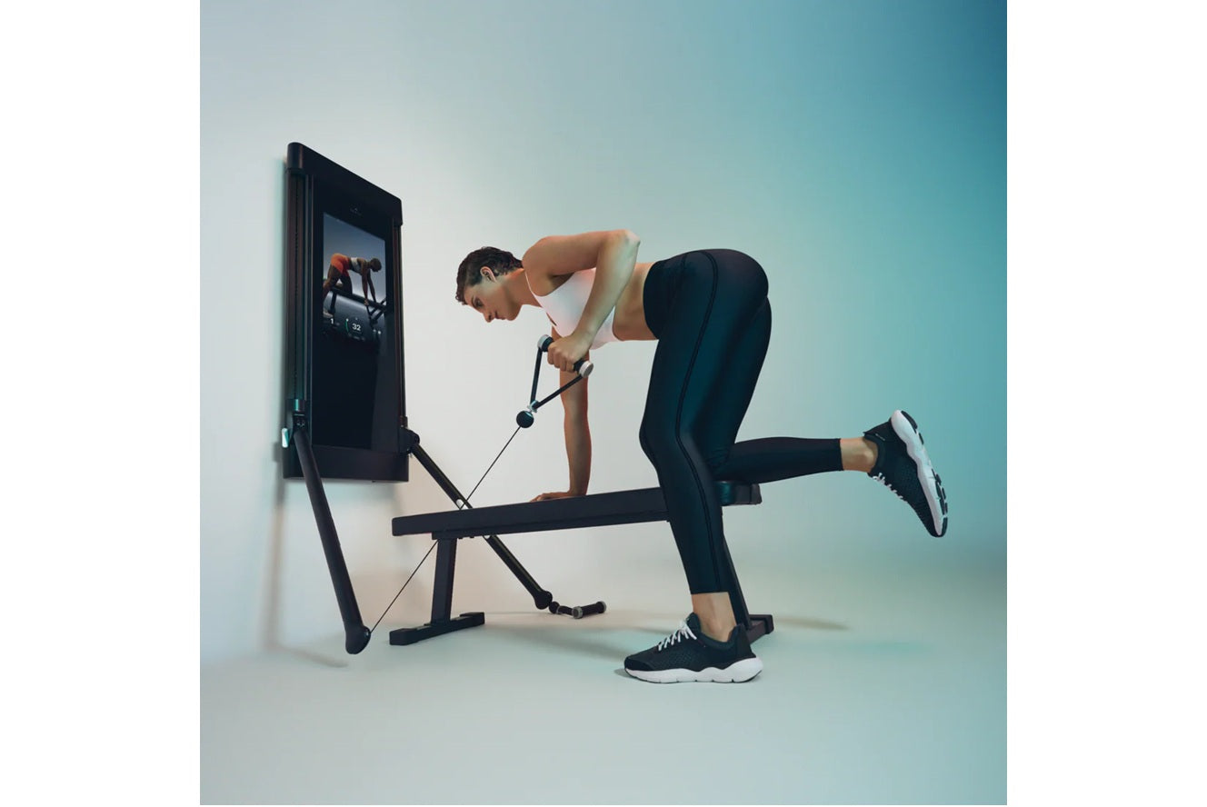 Man using black Tonal 2 Smart Home Gym with digital screen, performing resistance exercise on bench against blue gradient bac