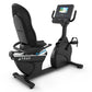 Black recumbent exercise bike with mesh backrest, digital display console, and foot pedals on white background