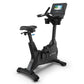 Black upright exercise bike with digital display console, padded seat, and handlebars on white background