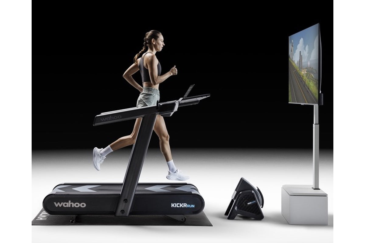Female runner on black Wahoo KICKR RUN smart treadmill with display screen showing cityscape, against black background
