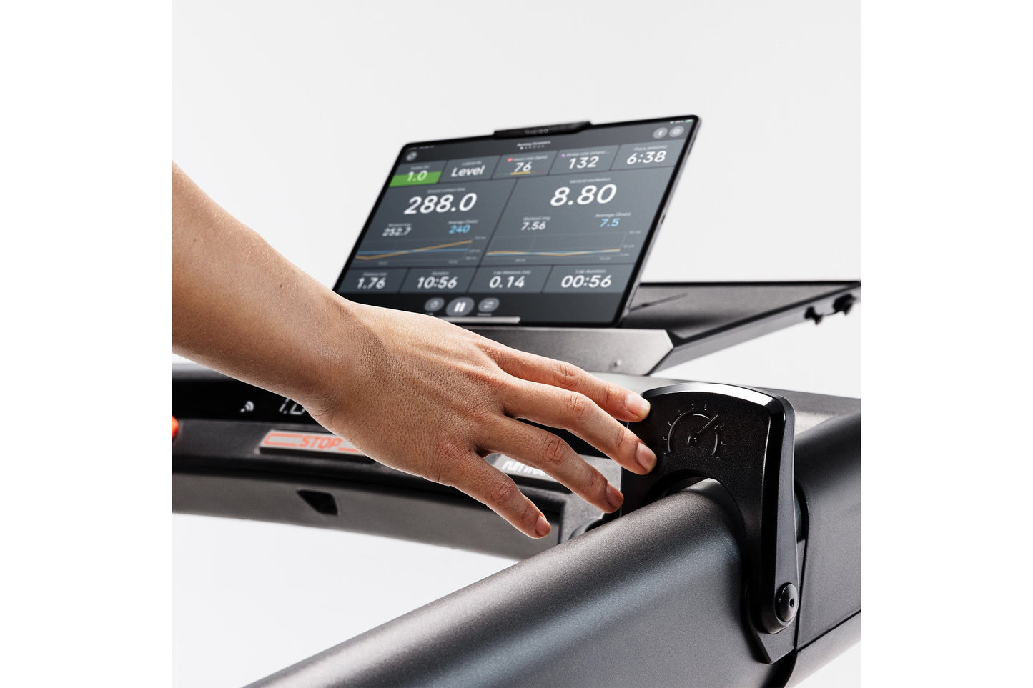 Hand operating black KICKR RUN smart treadmill console displaying workout metrics and digital display screen