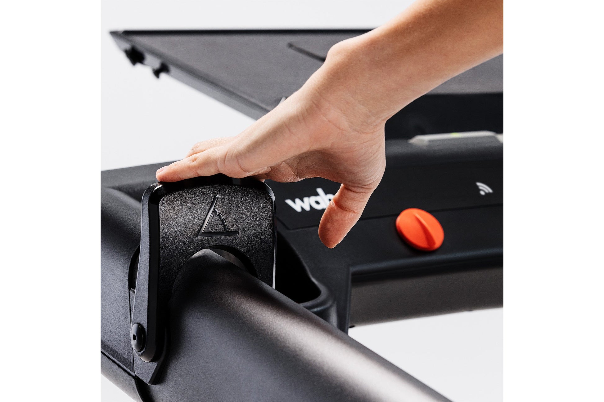 Hand adjusting black control knob on KICKR RUN smart treadmill with orange button visible
