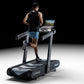 Man running on black and gray Wahoo KICKR RUN smart treadmill with laptop displaying scenic route on desk, worn by model on b