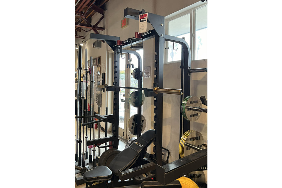 Warrior Elite 1.0 black squat rack with safety bars, weight plate storage, and padded seat in gym setting