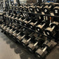Set of black 12-sided urethane dumbbells with white numbered labels ranging from 5 to 50 pounds, arranged on two-tier black m