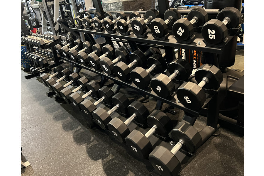 Set of black 12-sided urethane dumbbells with white numbered labels ranging from 5 to 50 pounds, arranged on two-tier black m