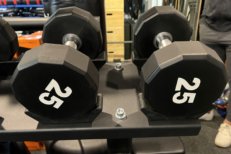 Pair of black 25-pound hexagonal dumbbells with white numbers on gray stand in gym setting