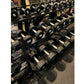 Black hexagonal urethane dumbbells arranged on tiered metal rack in gym setting, weights ranging from 5 to 50 pounds labeled 