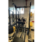 Black metal squat rack with yellow accents, vertical uprights, safety bars, and attached plate storage in gym setting