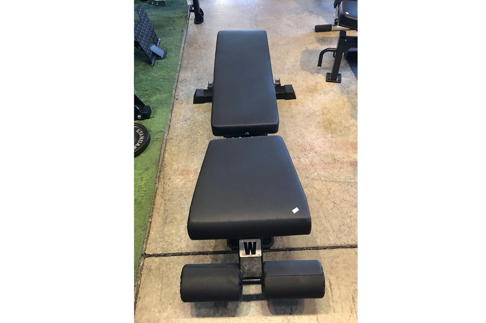 Black padded flat incline decline weight bench with adjustable backrest and leg extension, viewed from above on concrete floo