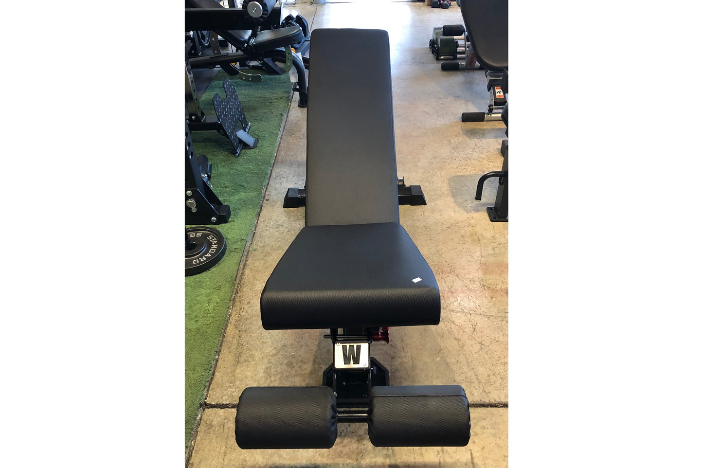 Black flat incline decline weightlifting bench with padded seat and back support, viewed from above in gym setting