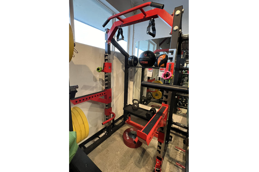 Red and black Warrior Elite 3.0 Power Rack with pull-up bar, weight plate storage, and resistance bands attached, displayed i