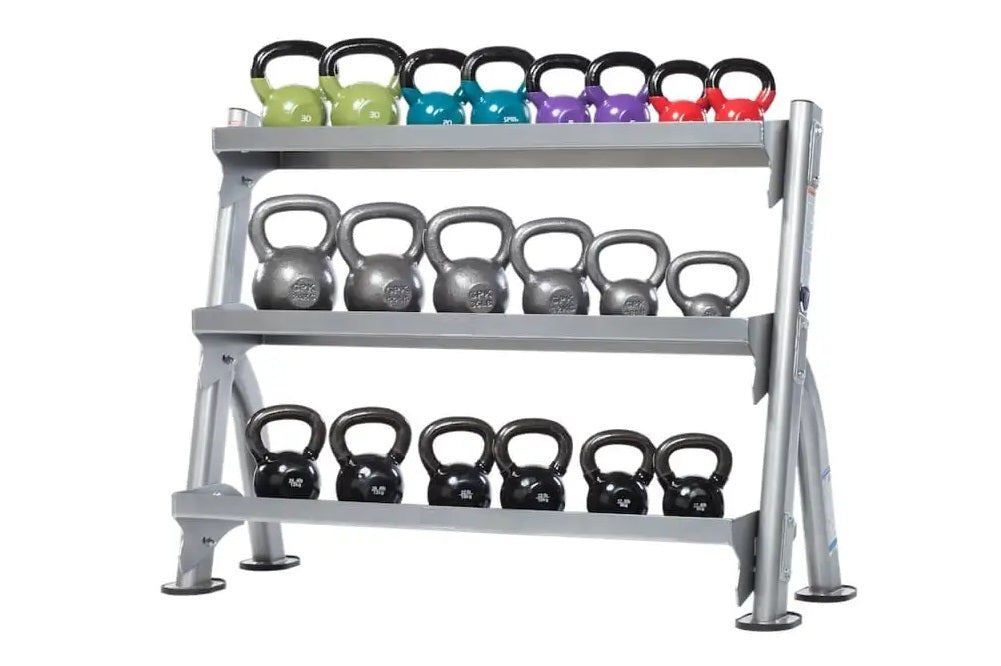 Three-tier gray steel kettlebell storage rack with black handles, holding colorful kettlebells in green, teal, purple, and re