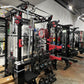 Black and red cable crossover power rack with dual pulleys, lat pulldown attachment, and kettlebell storage in gym setting