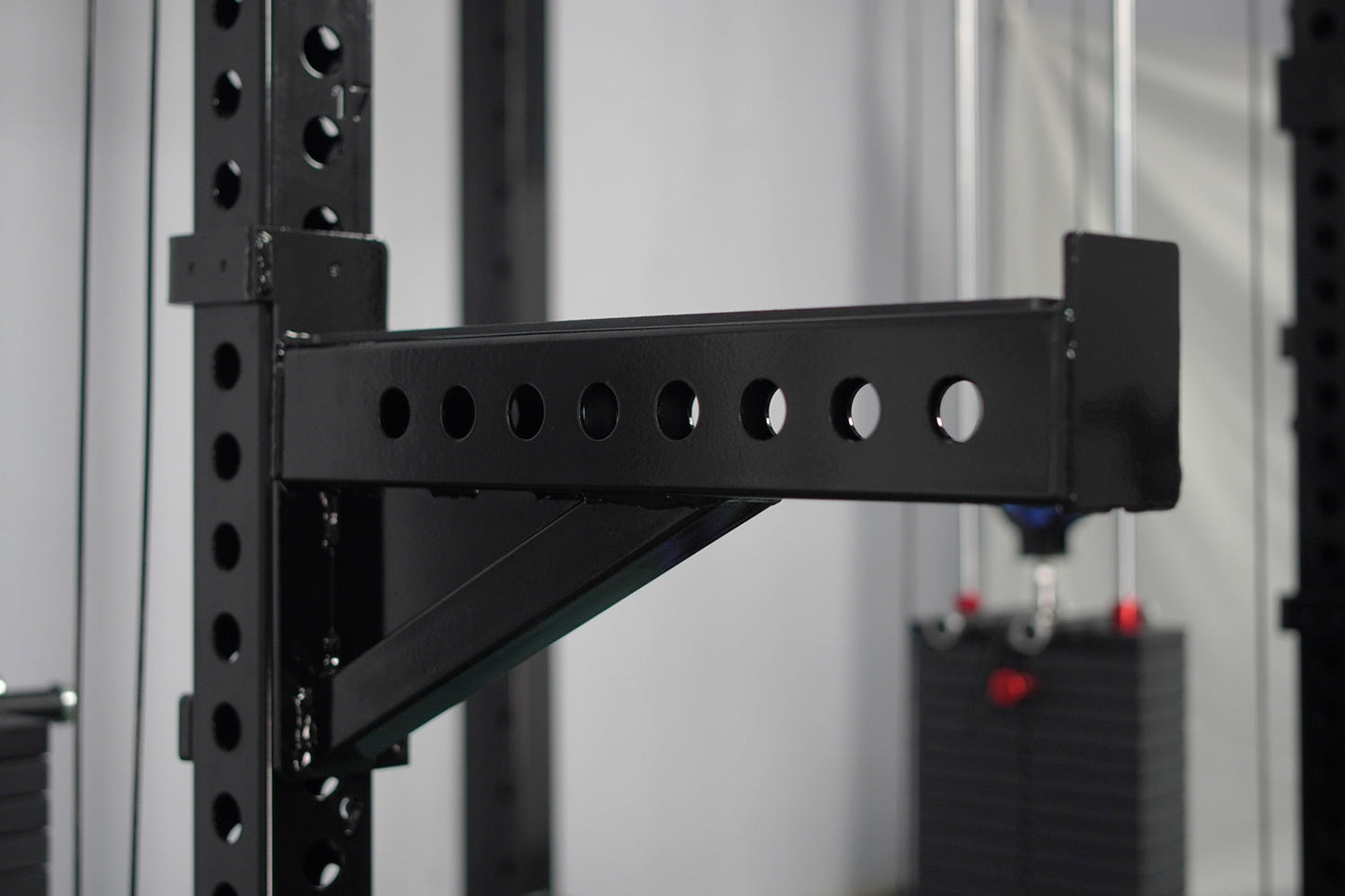 Black steel cable crossover pulley arm attachment with eight circular holes, mounted on perforated vertical posts with angled