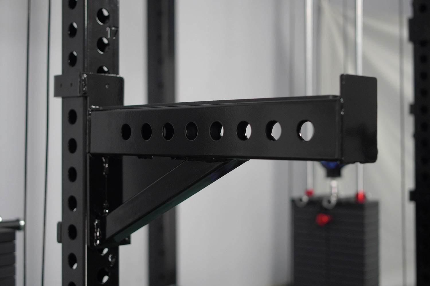 Black steel cable crossover pulley arm attachment with eight circular holes, mounted on perforated vertical posts with angled