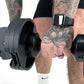 Man holding pair of black adjustable dumbbells with square buckle straps, wearing black shorts and white socks on white backg