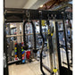 Black steel power rack with dual cable crossover stations, battle ropes, and smith cage in gym setting with colorful dumbbell