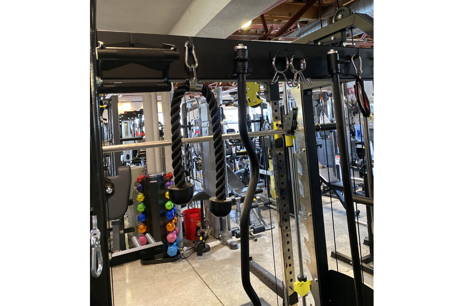 Black steel power rack with dual cable crossover stations, battle ropes, and smith cage in gym setting with colorful dumbbell