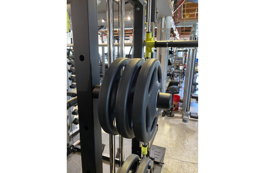 Black weight plates loaded on barbell of Warrior 701 all-in-one power rack with cable crossover in gym setting