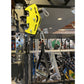 Bright yellow brake caliper with silver mounting hardware displayed on black power rack frame in gym showroom