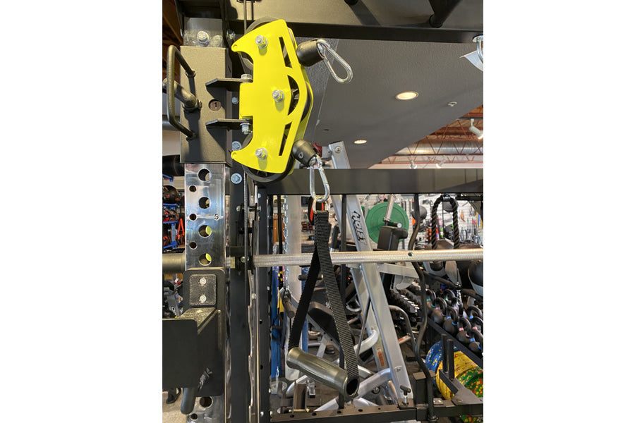 Bright yellow brake caliper with silver mounting hardware displayed on black power rack frame in gym showroom