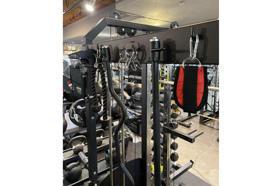 Black multi-functional power rack with integrated cable machine, red and black heavy bag, and weight storage in gym setting