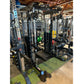 Black multi-functional power rack with cable pulleys, weight plates, and dumbbells on green and black gym flooring in warehou
