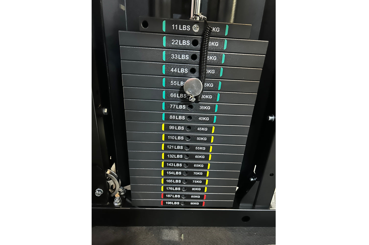 Warrior 901 power rack with stacked weight plates labeled 11 to 198 LBS, color-coded with teal, yellow, and red bands, chrome