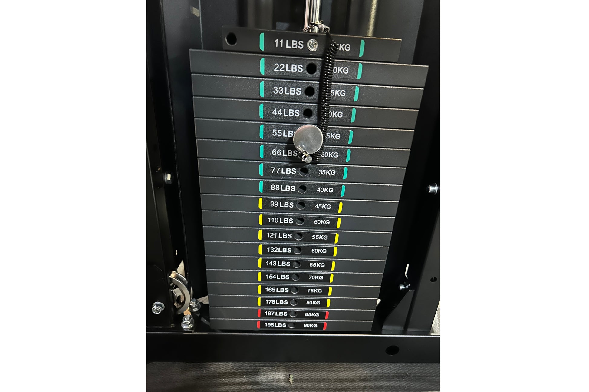 Warrior 901 power rack with stacked weight plates labeled 11 to 198 LBS, color-coded with teal, yellow, and red bands, chrome