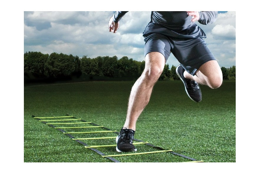 Athlete running through agility ladder on green synthetic turf field during daytime training