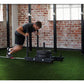 Man performing push exercise on black sled system with tire, on green turf in industrial gym space