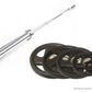 Weightlifting barbell with chrome shaft and black grip collar next to stack of black Olympic weight plates with center holes,
