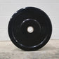Black rubber bumper plate with 25 lb weight marking on concrete floor against brick wall