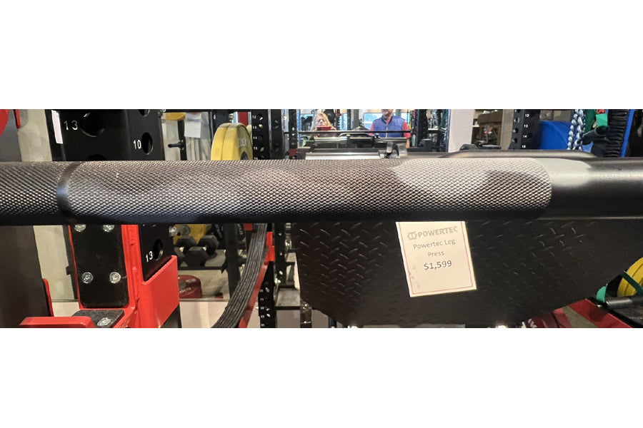Warrior Cerakote Powerlifting Bar in camo finish with knurled grip, displayed on black diamond plate rack in gym setting