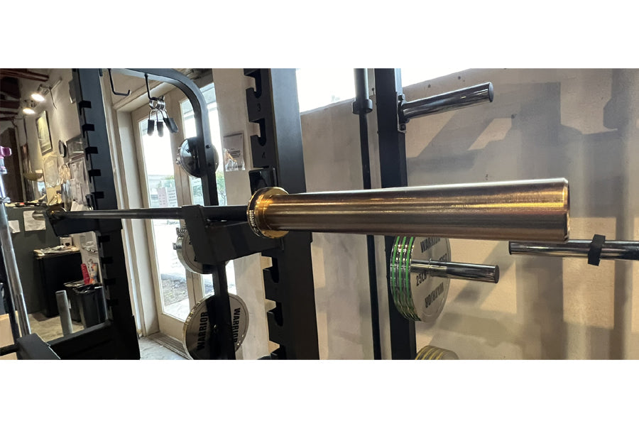 Warrior Black Cerakote & Gold Titanium Barbell with black power rack frame and weight plates