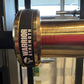 Warrior Strength black cerakote and gold titanium barbell with red and gold striped sleeve, displayed in gym setting