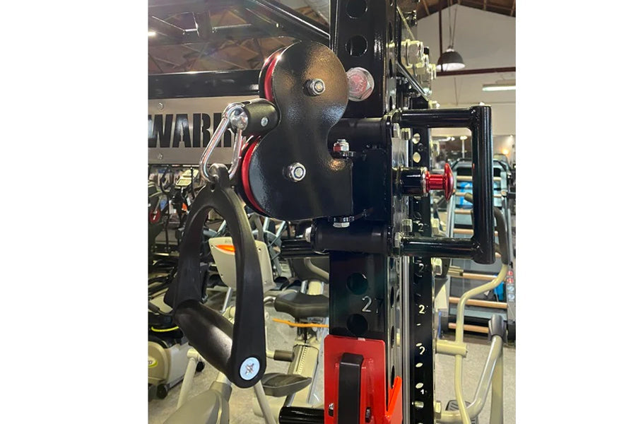 Warrior 3.0 cable crossover pulley system with black pulleys, red accents, and lat pulldown attachment in gym setting