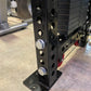 Black steel weight stack machine with multiple circular holes and chrome adjustment pins, displayed in gym setting