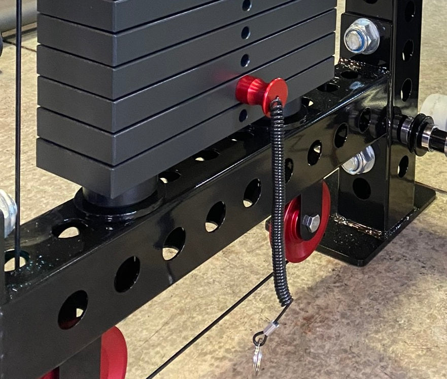 Black steel lat pulldown machine with red handles, weight plates stacked on rear post, and chrome adjustment knobs on concret