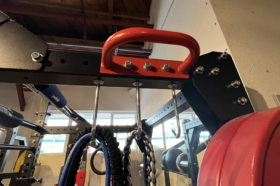 Red and black power rack with red handle bar, silver bolts, and hanging resistance bands in gym setting