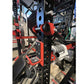 Red and black weightlifting cage with numbered attachment points, featuring pull-up bar and plate storage, in gym setting